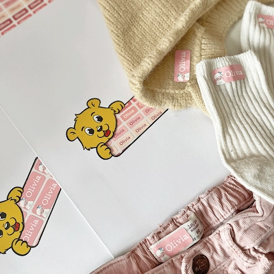 Pull jaune, chaussettes blanches et pantalon rose avec des étiquettes thermocollantes roses au prénom Olivia